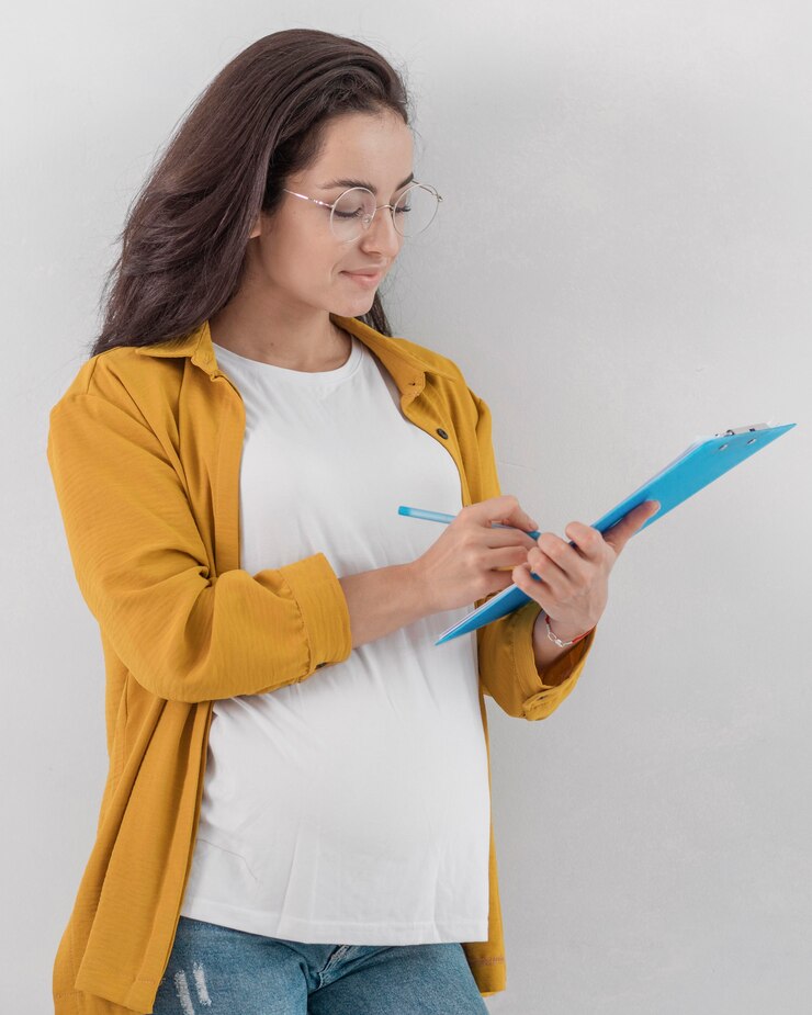 Foto grátis mulher grávida segurando uma prancheta e escrevendo com uma caneta