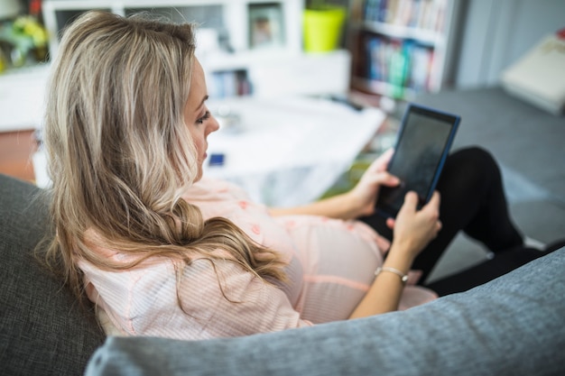 Mulher grávida, sentar sofá, usando, tablete digital
