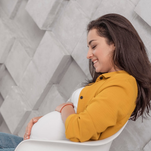Mulher grávida sorridente em casa abraçando a barriga