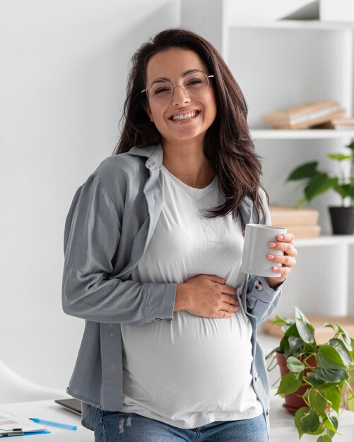Mulher grávida sorridente em casa com uma caneca de café
