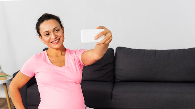 Foto grátis mulher grávida sorridente fazendo selfie em casa durante o treinamento