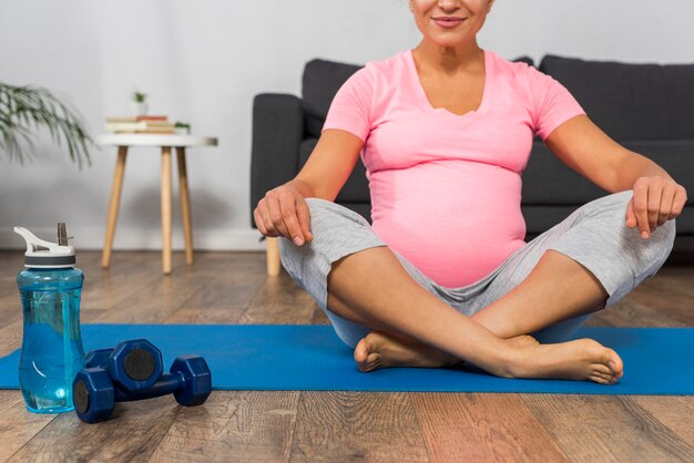 Mulher grávida sorridente na esteira de exercícios em casa com pesos e garrafa de água