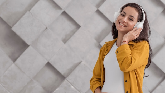 Mulher grávida sorridente ouvindo música em fones de ouvido com espaço de cópia