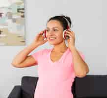 Foto grátis mulher grávida sorridente ouvindo música em fones de ouvido enquanto se exercita em casa