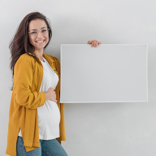 Mulher grávida sorridente segurando um quadro branco