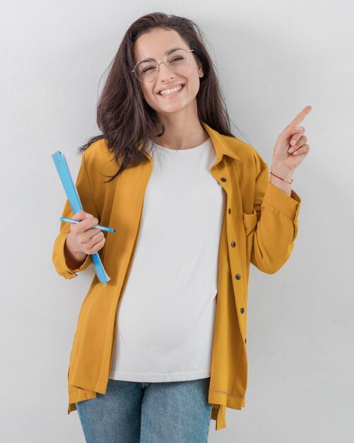 Mulher grávida sorridente segurando uma prancheta e apontando para cima