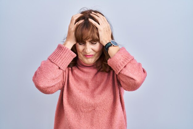 Mulher hispânica de meia-idade em pé sobre fundo isolado sofrendo de dor de cabeça desesperada e estressada porque dor e enxaqueca. mãos na cabeça.