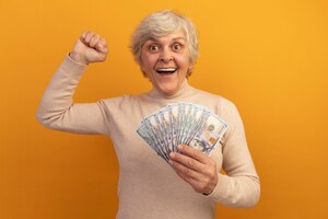 Mulher idosa alegre usando um suéter cremoso de gola alta e segurando dinheiro para levantar o dinheiro