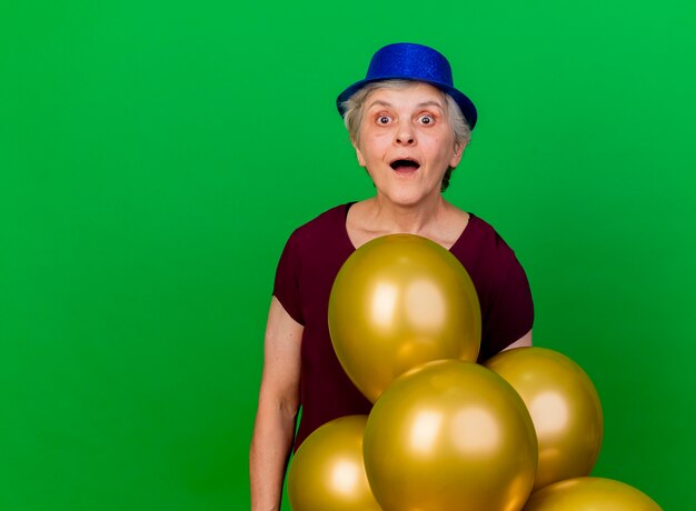 Mulher idosa animada usando chapéu de festa em pé com balões de hélio em verde
