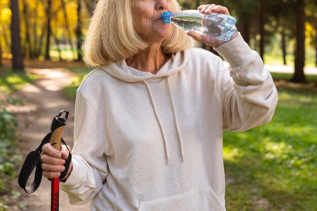 Mulher idosa ao ar livre bebendo água durante uma caminhada