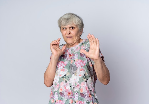 Mulher idosa descontente em pé com as mãos levantadas, isoladas na parede branca