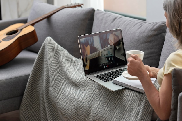 Mulher idosa em casa no sofá usando laptop e tomando café