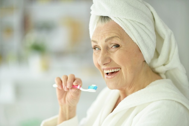 Mulher idosa escovando os dentes no banheiro