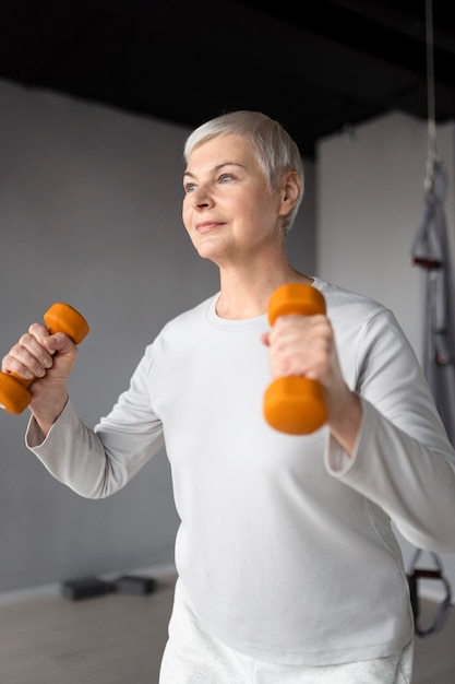 Mulher idosa fazendo exercícios com halteres na academia