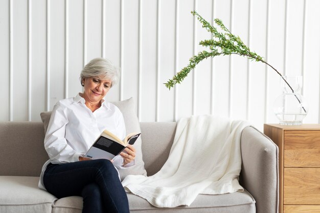 Mulher idosa lendo um livro no sofá em uma sala de estar com decoração escandinava