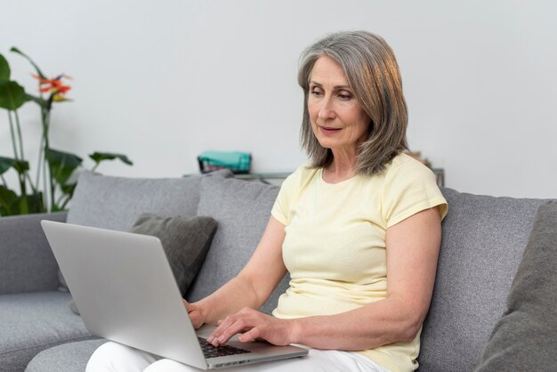 Mulher idosa no sofá em casa usando laptop