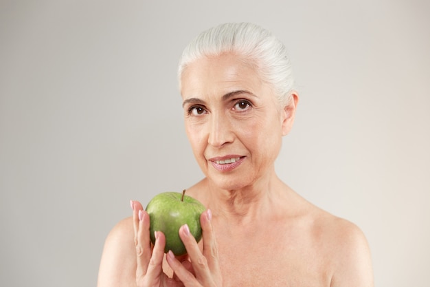 Mulher idosa nua concentrada segurando a maçã.