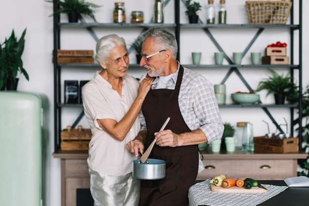 Mulher idosa olhando para o marido preparando comida na cozinha