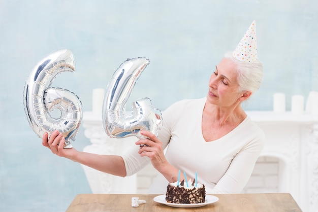 Mulher idosa que olha o balão da folha de prata em seu 64th aniversário
