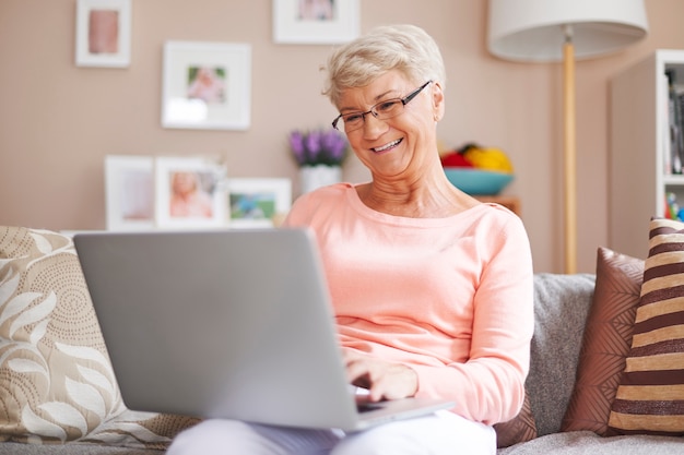 Mulher idosa relaxando com laptop no sofá