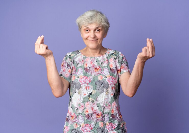 Foto grátis mulher idosa satisfeita gesticulando sinal de dinheiro com as duas mãos isoladas na parede roxa