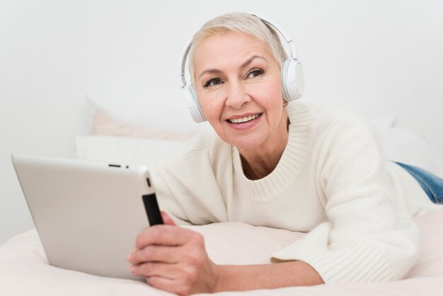 Mulher idosa sorridente com fones de ouvido segurando o tablet