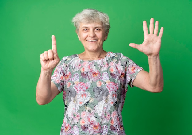 Mulher idosa sorridente gesticula seis com as mãos isoladas na parede verde