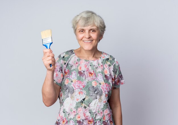 Mulher idosa sorridente segurando pincel isolado na parede branca