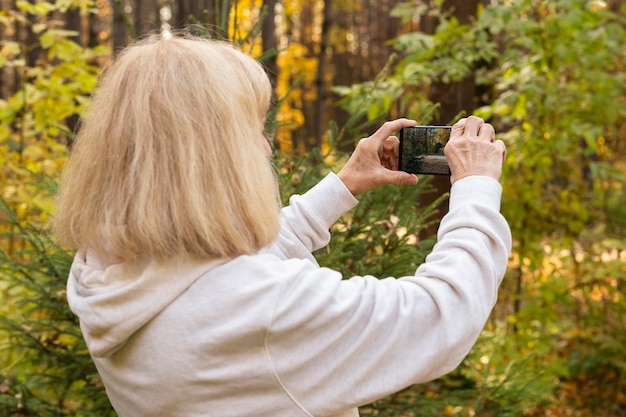 Mulher idosa usando smartphone para tirar fotos da natureza