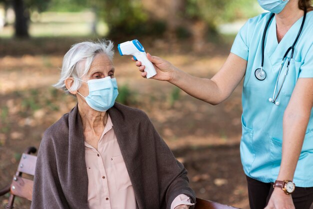 Mulher idosa verificando a temperatura pela enfermeira