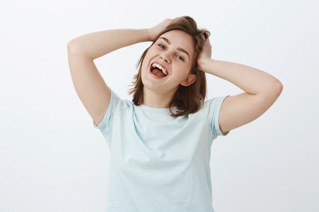 Mulher indo às compras, sentindo-se animada e satisfeita, finalmente, recebendo o pagamento. Retrato de uma garota atraente alegre e despreocupada tocando e bagunçando o cabelo, sorrindo amplamente de emoções positivas