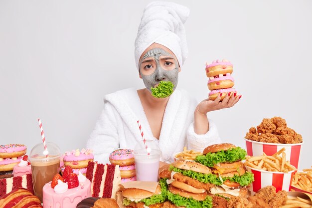 Mulher infeliz se sente cansada de comer restrições mantém a dieta segura pilha de rosquinhas deliciosas e apetitosas tem boca entalada com salada verde evita fast food fastidioso