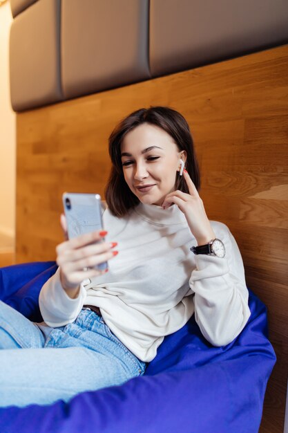 Mulher interessante está sentado na cadeira violeta brilhante usando seu telefone para mensagens de texto com seus amigos