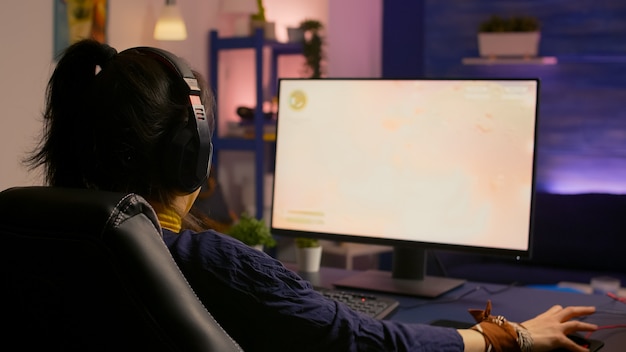 Mulher jogadora concentrada perdendo jogo multijogador virtual em um computador potente em casa com fones de ouvido profissionais