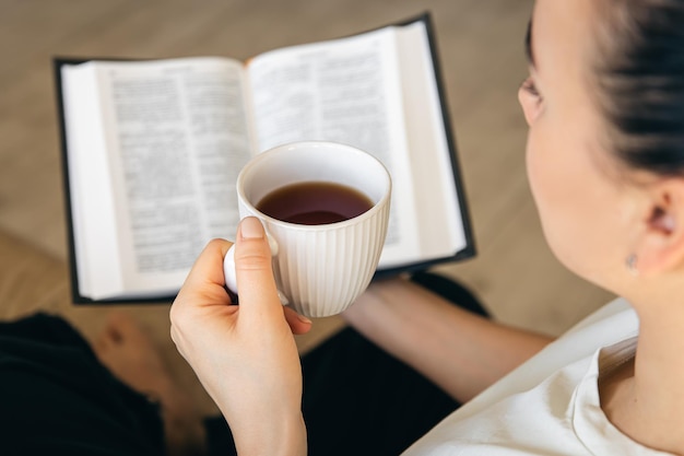 Foto grátis mulher jovem a beber chá quente e a ler o livro de papel favorito