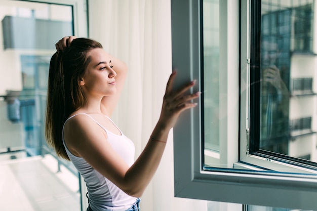 Mulher jovem abre uma janela de plástico para tomar ar fresco e sorrir em casa