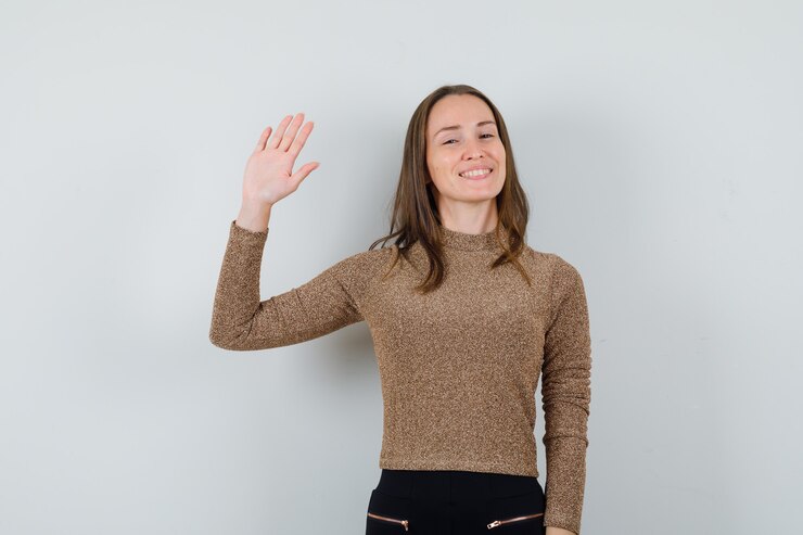 Foto grátis mulher jovem acenando com a mão para se despedir com uma blusa dourada e parecendo focada