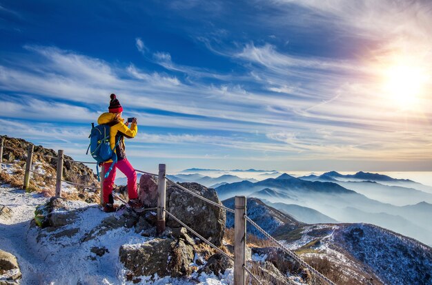 Mulher jovem alpinista tirando foto com smartphone no pico de montanhas no inverno