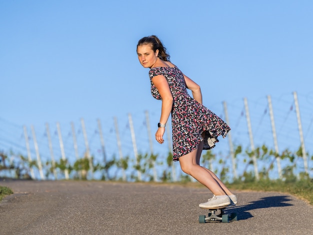 Mulher jovem andando de skate em uma estrada vazia cercada por vegetação