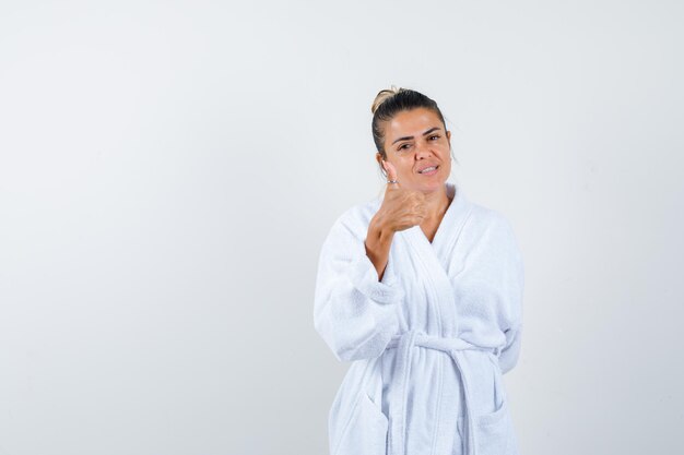 Mulher jovem aparecendo com o polegar no roupão de banho e parecendo alegre