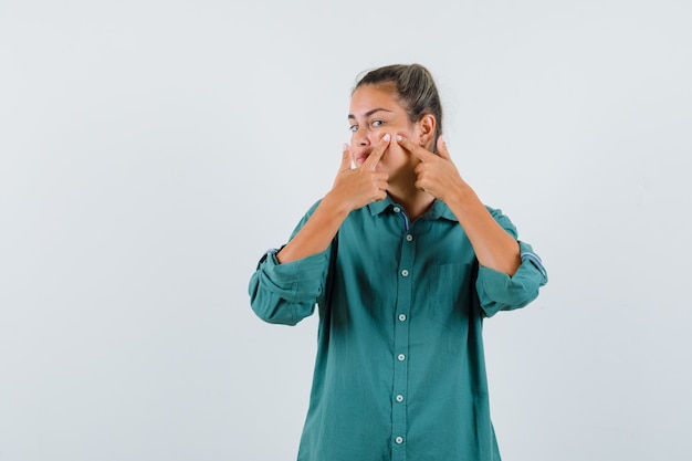 Foto grátis mulher jovem apertando espinha em uma blusa verde e parecendo focada