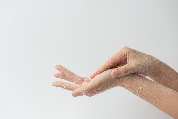 Mulher jovem aplicando esfoliante natural de limão nas mãos contra uma superfície branca