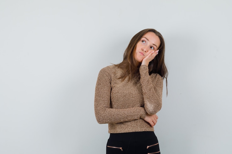 Foto grátis mulher jovem apoiada na mão com uma blusa dourada e parecendo entediada