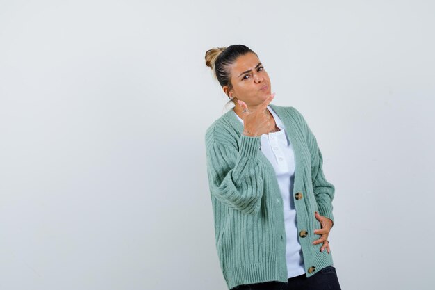 Mulher jovem apontando para a direita com o dedo indicador, segurando a mão na cintura em uma camisa branca e um casaco de lã verde menta e parecendo feliz