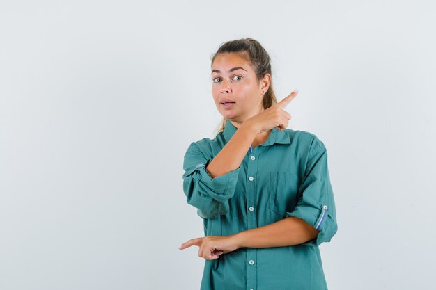 Mulher jovem apontando para diferentes direções com o dedo indicador em uma blusa verde e atraente