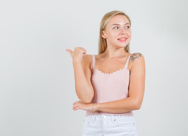 Mulher jovem apontando para o lado com o polegar na camiseta