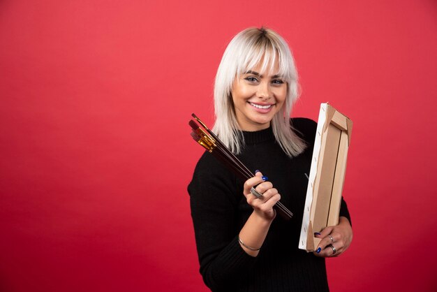 Mulher jovem artista segurando materiais de arte em uma parede vermelha.