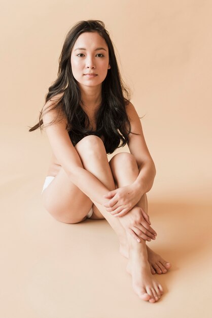 Mulher jovem asiática em roupa interior sentada com as pernas cruzadas