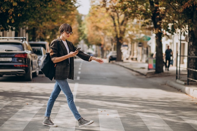 Mulher jovem atravessando uma rua usando o telefone