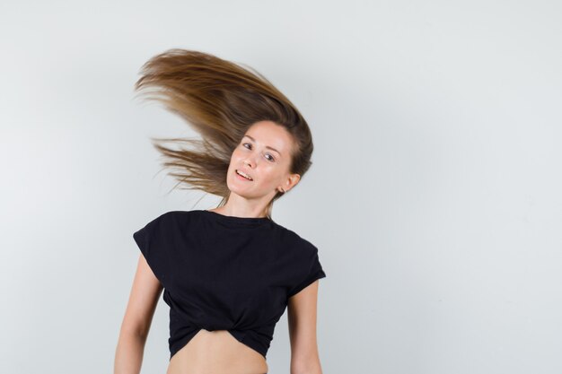 Foto grátis mulher jovem balançando o cabelo com uma blusa preta e parecendo relaxada